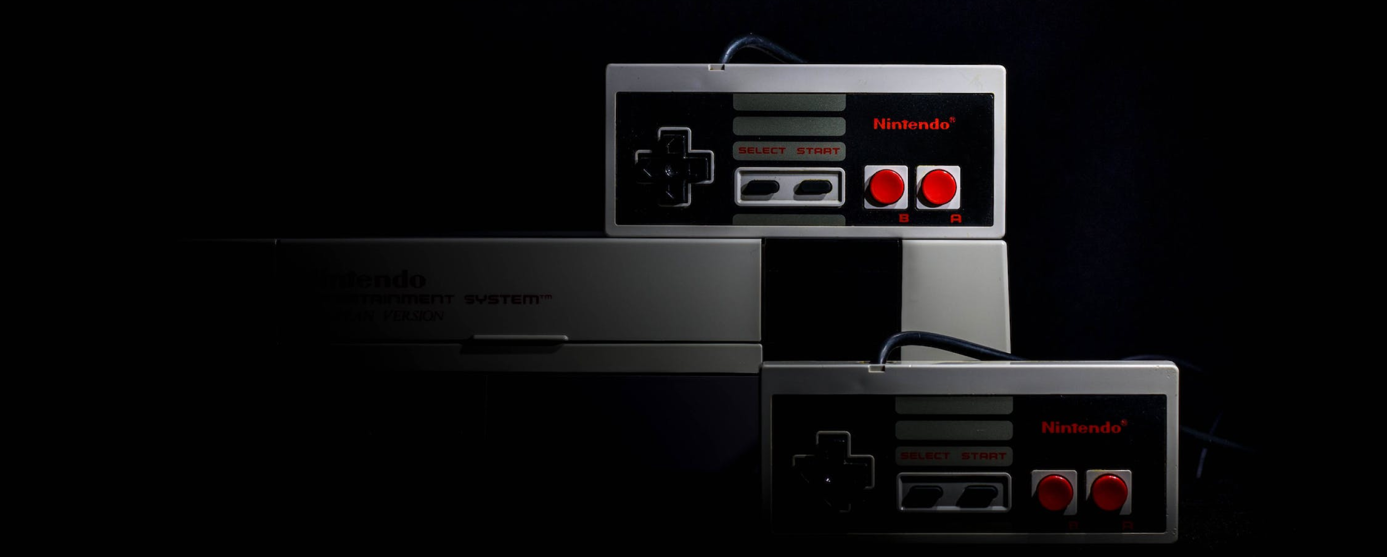 The original Nintendo Entertainment System (NES) captured with two controllers and the console in a dark setting.